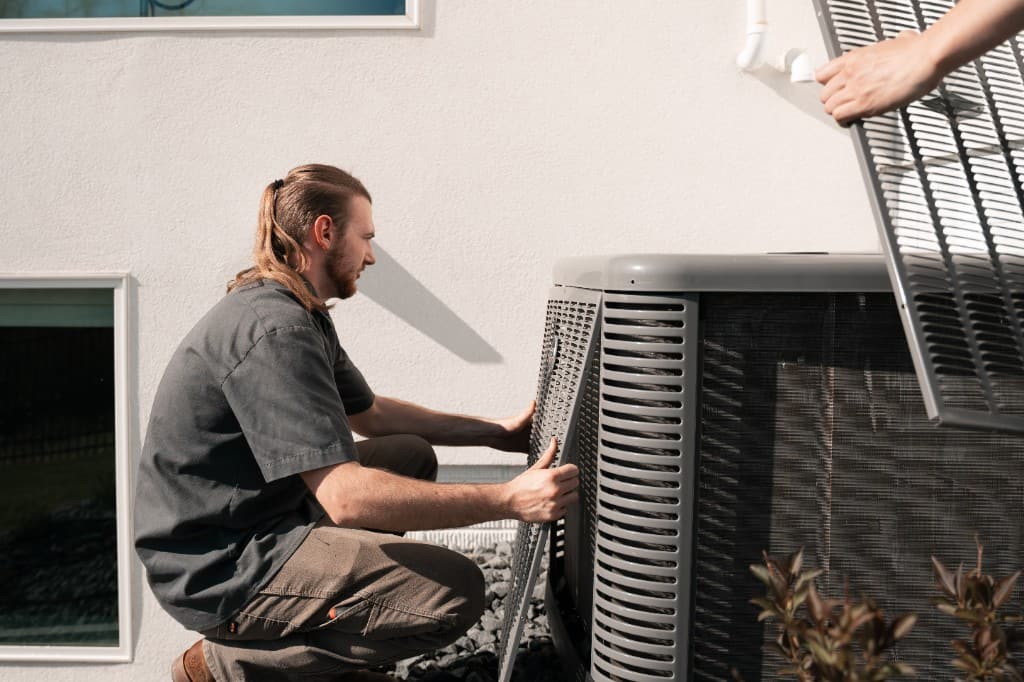 An All Seasons HVAC technician removing the access panel of an outdoor air-conditioning condenser unit at a home